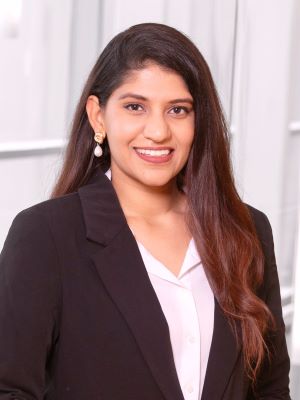 A woman with long brown/red hair in a black blazer with a white shirt smiles in a professional photo