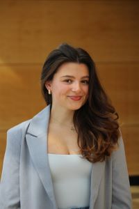 Photo of Bizzy Webb, Michigan Ross BBA student wearing a light blue suit jacket with a white shirt and with long dark curly hair