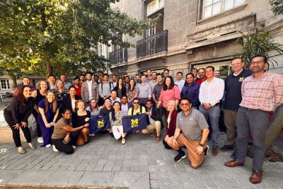 Group photo of Michigan Ross Online MBA students and faculty holding a maize and blue Michigan Ross flag. 