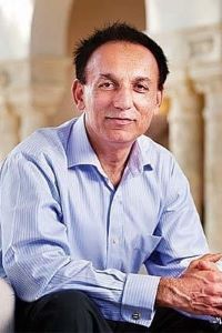 Photo of Bharat Desai with dark hair wearing a light blue button up shirt. 