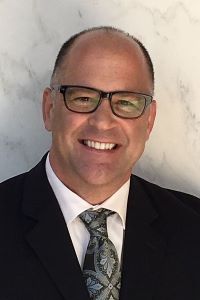 Photo of Jerry White smiling and wearing a black suit with a white shirt and a patterned tie. 