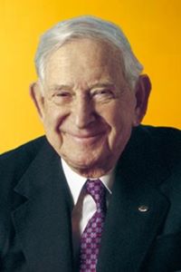 Photo of a man with white hair smiling and wearing a navy blue suit.