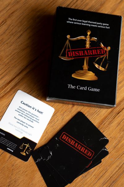 Cards that say "Disbarred" on the back lay scattered on a wood table beside the box for the card game.