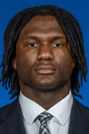 Man with long dark hair wearing a dark suit with a white shirt and a Michigan tie