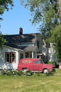 Photo of an old red truck outside of a white house at the Dixboro Project property in Plymouth Michigan.