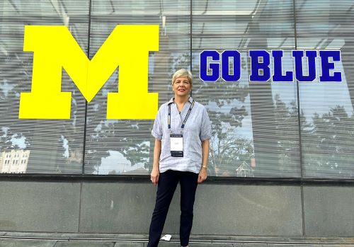 Elaine standing in front of the Ross School of Business in front of a "Go Blue" decal on the windows