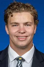 Man with blond curly hair wearing a dark suit with white shirt and Michigan tie