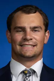 Man with dark hair wearing a dark suit with white shirt and a Michigan tie