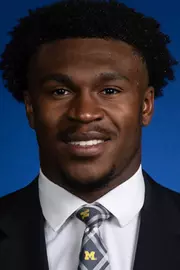 Man with dark hair wearing a dark suit and white shirt with Michigan tie