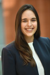 Photo of a woman with long dark hair smiling and wearing a blue suit jacket with a white shirt