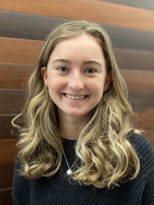 Presley Snyder smiles for a headshot with a wood panel background behind her.