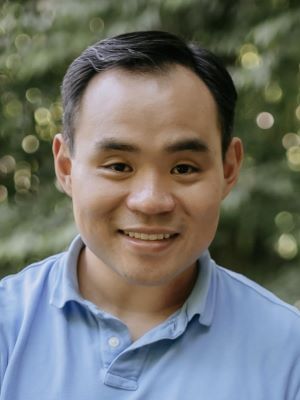 Man with dark hair wearing a blue shirt and smiling