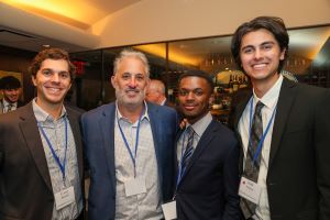 Group of four male representatives from the Ross School of Business standing and wearing suits and smiling in New York City.  