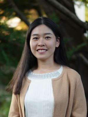 Woman with long dark straight hair wearing a brown sweater with a white shirt and smiling