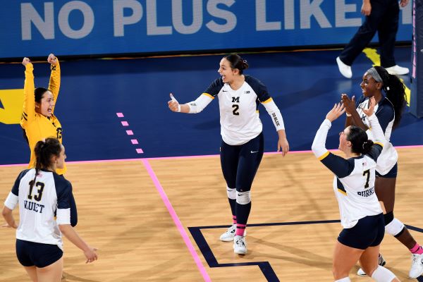 A woman on a wood floored court in a volleyball jersey/outfit cheering with her teammates