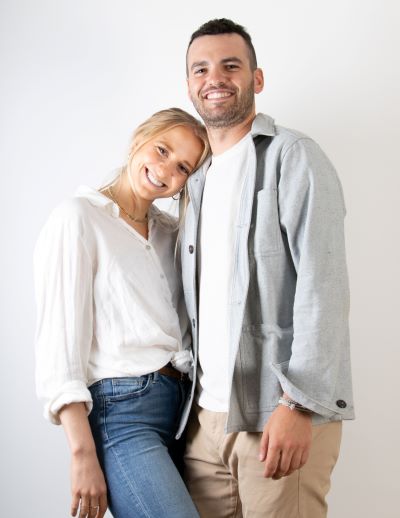 A man and woman stand side by side smiling in front of a white background