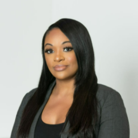 Crystal smiles, wearing a gray blazer and black shirt and stands in front of a white background