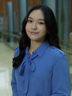 A woman with long black hair smiling, wearing a light blue shirt with a bow around the collar