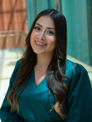 A woman with long brown hair smiling, wearing a teal shirt