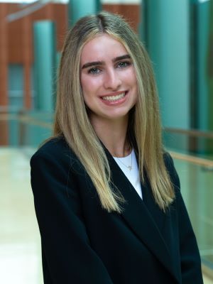 A blonde woman in a black suit with white shirt smiles in the Winter Garden of the Michigan Ross building