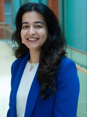 A woman with long dark brown hair smiles wearing a blue blazer jacket and white shirt in the Ross Winter Garden