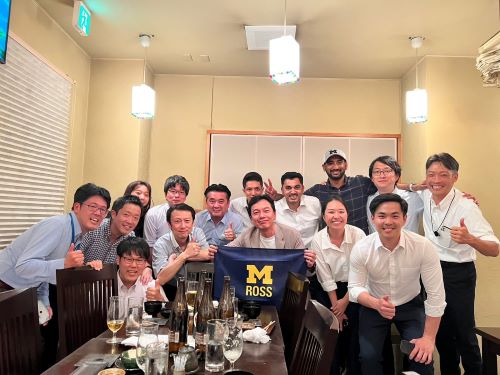 A group of Ross students posing around a table with the Ross flag.