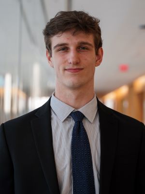 A man wearing a black suit with pinstriped shirt and blue tie