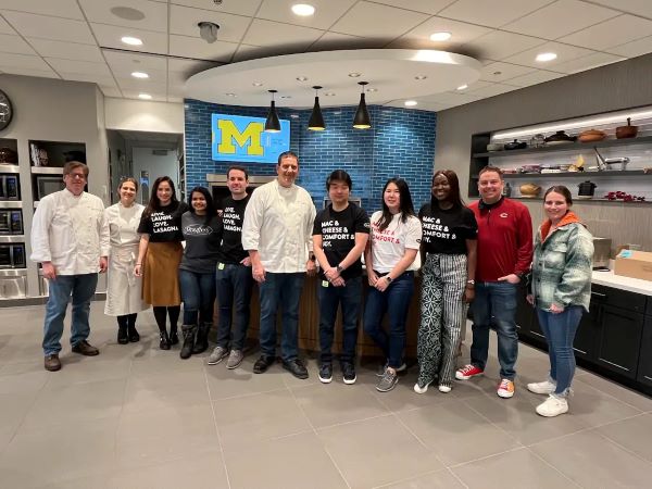 Students stand with chefs in a large well appointed kitchen.