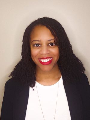 Olivia smiles in a black blazer with a white shirt in front of a beige background