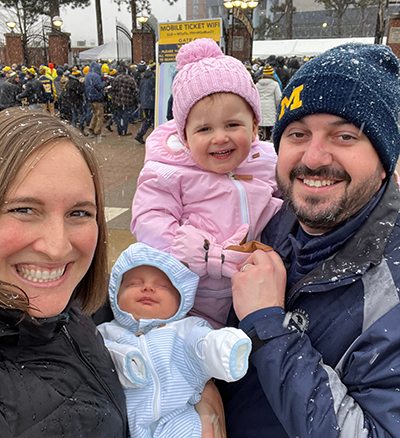 Heydlauff poses with her husband and two young children in the snow in front of a Michigan sporting event