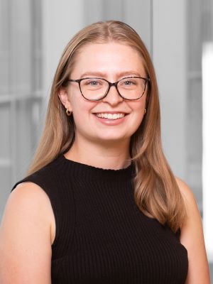 A woman with shoulder-length blonde hair and glasses wearing a professional black top smiles in a headshot photo inside the Ross building