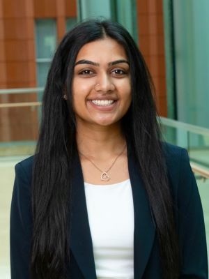 Rujula Lna poses in a navy blazer in front of a background of the Ross Winter Garden