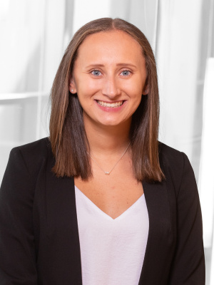 A woman with shoulder length brown hair smiles, wearing a black blazer and white shirt