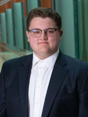 Scott wears a dark blue/black suit, standing in the Ross Winter Garden