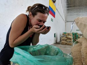 A woman smells coffee beans in a warehouse filled with bags of coffee beans