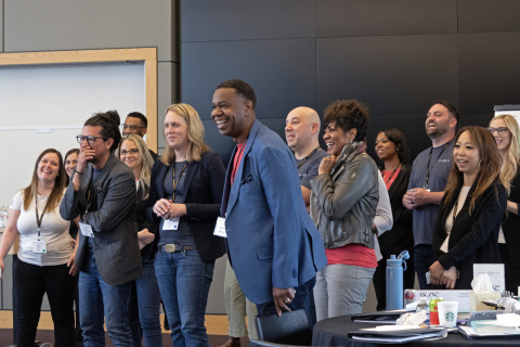 A crowd of Stellantis employees standing in a conference room smile and laugh while engaged in class.