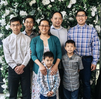 Family of 7 poses in front of flowers for photo.