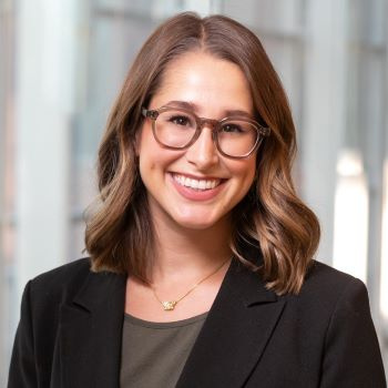 Woman in black blazer with brown hair and glasses smiling