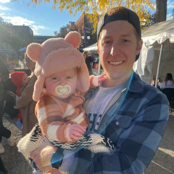 Man holding baby in pink animal hat.