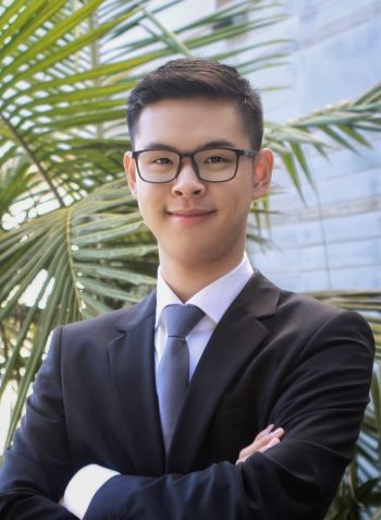 A man with glasses in a suit smiles in this professional headshot