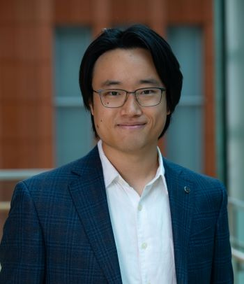 A man in a blue blazer with glasses smiles in a professional headshot photo