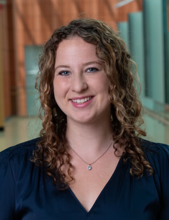 A woman in a blue dress shirt with curly hair smiles in a professional headshot photo