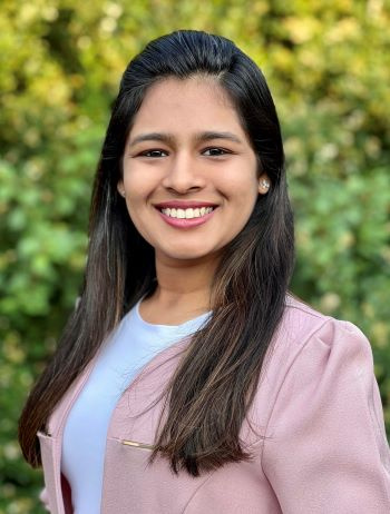 A woman with dark hair and a pink blazer smiles in a professional headshot photo