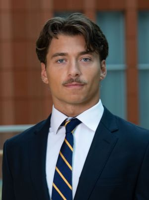 Man in blue suit with brown hair in front of Ross building