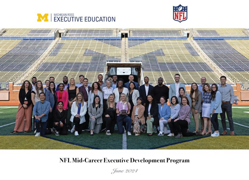 A diverse group of participants pose on the field of the Michigan Stadium