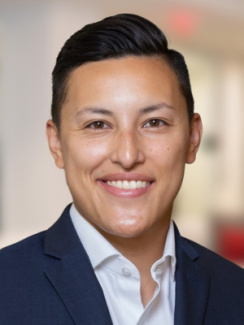 Rachel smiles, wearing a dark blue blazer and white dress shirt.