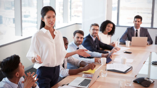 Woman talking to group of executives at a long table