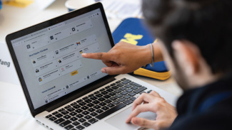 A student looks at a laptop screen as someone points to something on it