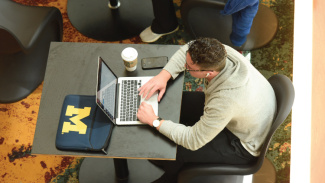 A student typing on a laptop computer at a small table in the Ross Winter Garden