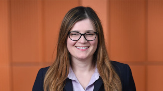 Photo of Michigan Ross Online MBA student Vanda Ametlli wearing a black suit with a purple shirt with long hair and glasses. 